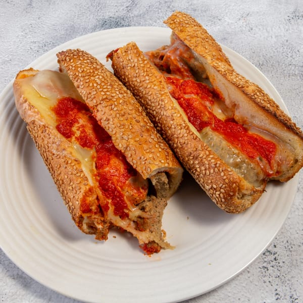 Two meatball subs with melted cheese and red sauce on sesame seed rolls, on a white plate.