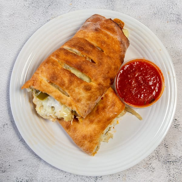 Golden-brown calzone with melted cheese and green peppers, served with a side of red marinara sauce.
