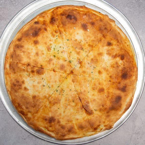 Golden-brown baked flatbread, cut into wedges, topped with herbs and salt on a metal pizza pan.