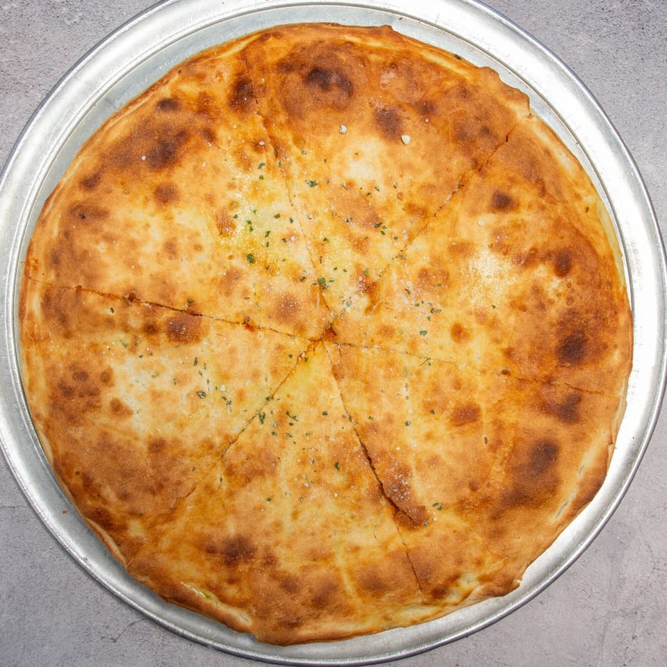 Golden-brown baked flatbread, cut into wedges, topped with herbs and salt on a metal pizza pan.