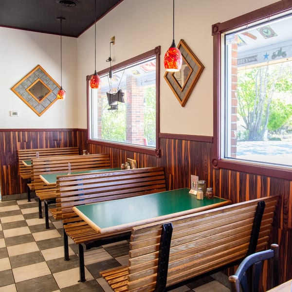An empty restaurant dining room with wooden booths, green tables, and a checkered floor.