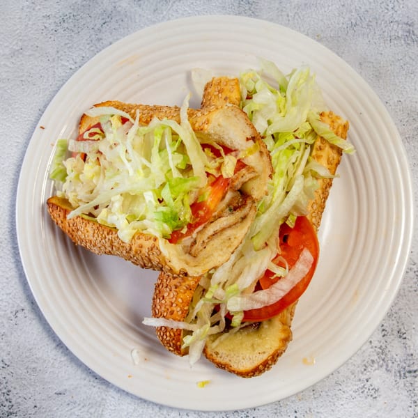 Two halves of a sesame seed sub sandwich filled with meat, cheese, lettuce, and tomatoes on a white plate.