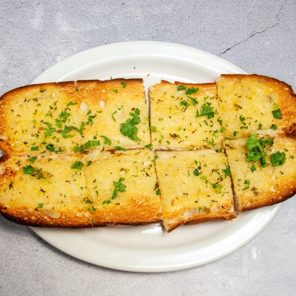 Golden-brown garlic bread, cut into pieces and garnished with fresh parsley, on a white plate.