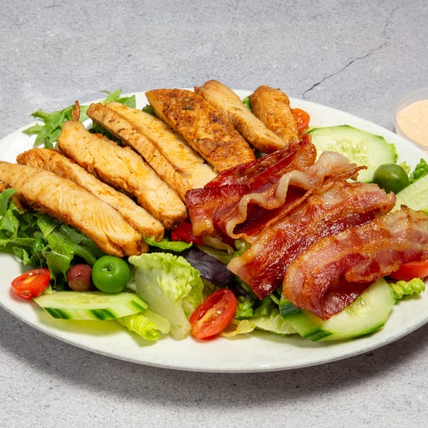 A vibrant salad with grilled chicken strips, crispy bacon, fresh greens, cucumber, tomatoes, and olives.