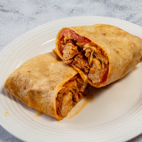 Two halves of a chicken wrap with tomatoes and sauce, on a white plate.