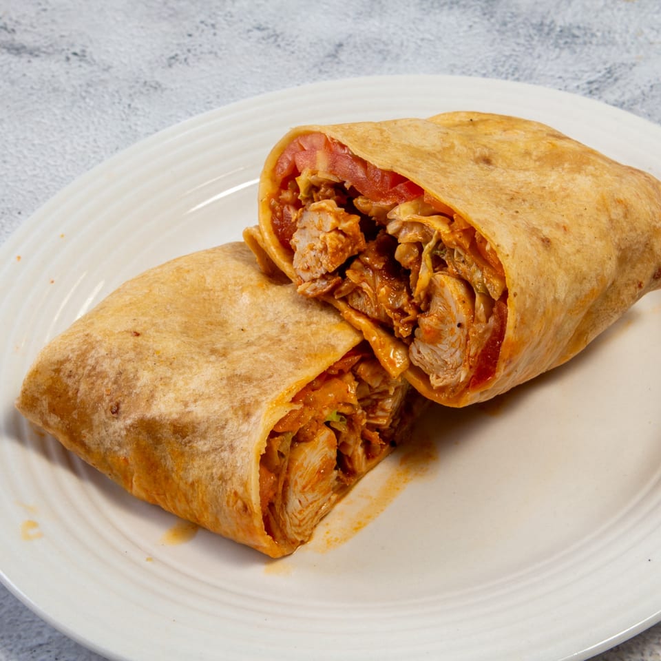 Two halves of a chicken wrap with tomatoes and sauce, on a white plate.