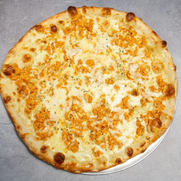 A whole round buffalo chicken pizza with white cheese and orange chicken pieces on a metal pan.