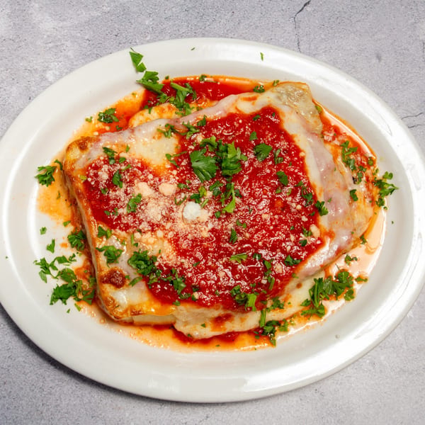 Baked ravioli topped with red sauce, melted cheese, grated Parmesan, and fresh parsley on a white plate.